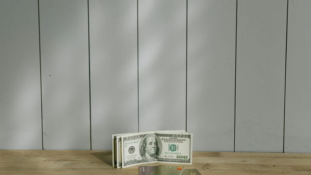 A stack of hundred-dollar bills and credit cards on a wooden surface with a neutral background.