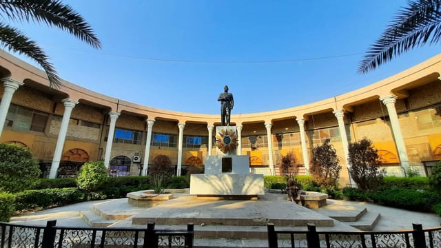 Elegant colonnaded courtyard featuring a prominent statue under a clear blue sky in Baghdad.