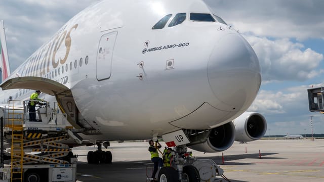 An Airbus A380-800 aircraft being serviced on airport tarmac under a bright sky.