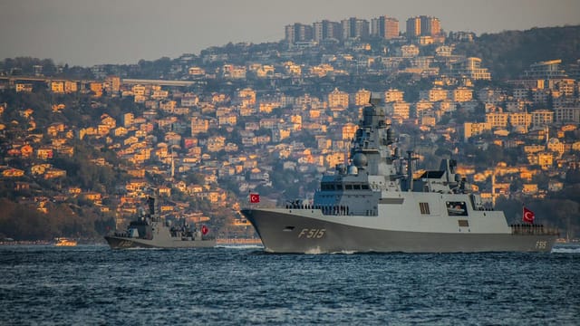 Turkish navy warships sail through the Bosphorus, framed by Istanbul's hillside residences.
