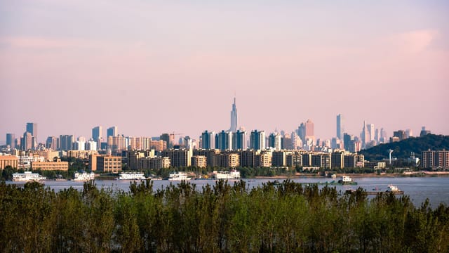 Panoramic view of a vibrant city skyline across a tranquil river during daytime.