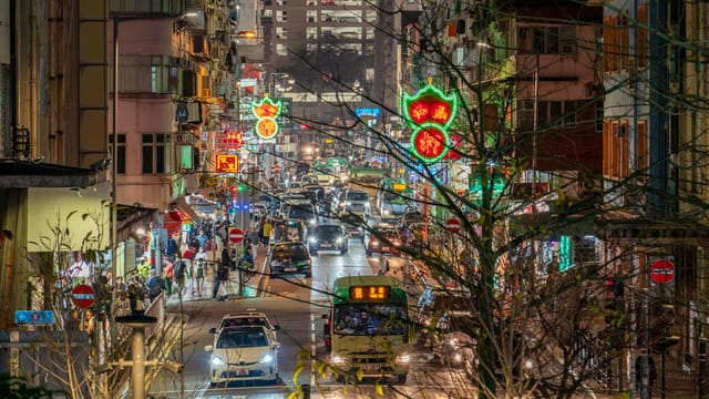 Vibrant city street illuminated by neon lights, buzzing with nighttime traffic and activity.