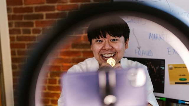 Excited Asian man presenting lively Bitcoin discussion with a smile indoors.