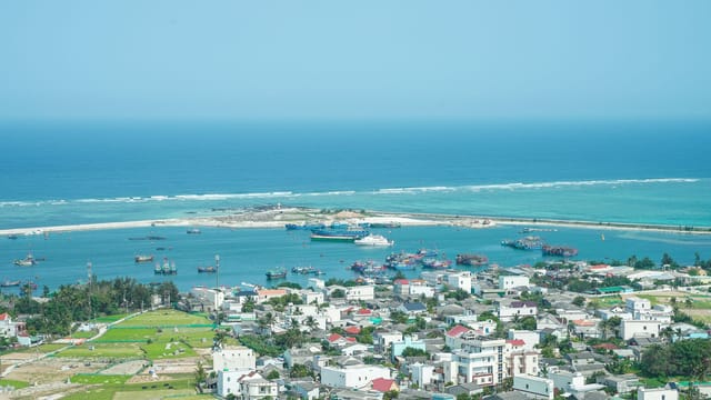 Aerial view of Ly Son Island harbor with boats and vibrant buildings, showcasing the tranquil turquoise sea.