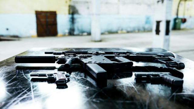 Various firearms displayed on a scratched metal table in an industrial setting.