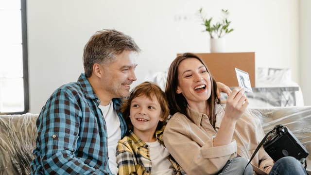 A cheerful family enjoys time together on a couch surrounded by moving boxes in their new home.