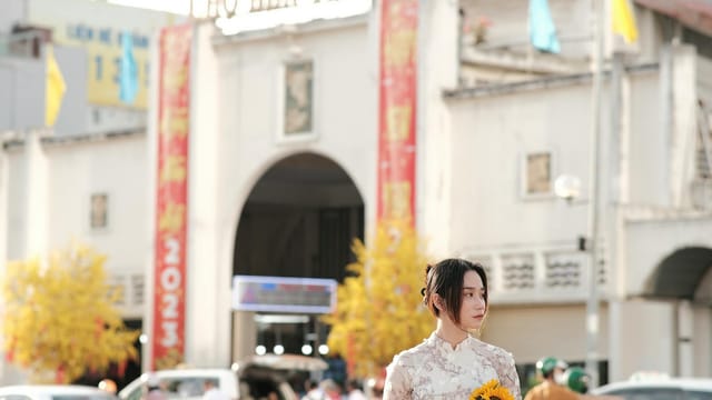 Woman in traditional dress holding sunflowers in front of Bến Thành Market, Ho Chi Minh City.