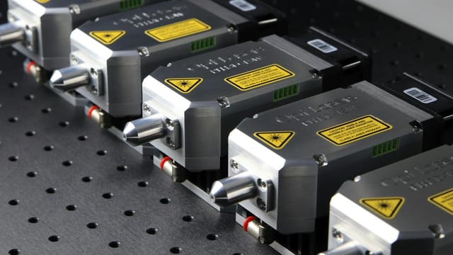 Detailed close-up of industrial laser modules with warning labels on a perforated metal surface.