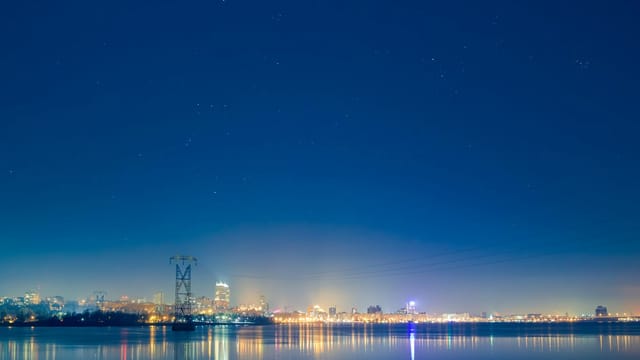 Illuminated cityscape of Dnipro at night with stars reflecting over calm water.