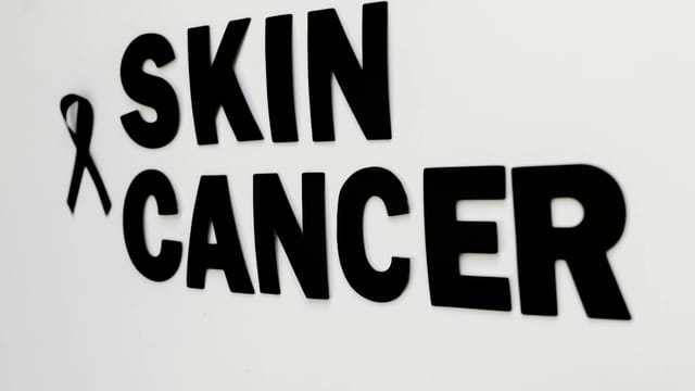 Close-up of black text and awareness ribbon highlighting skin cancer awareness.
