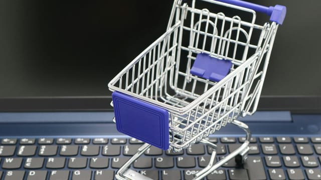 A mini shopping cart placed on a laptop keyboard, symbolizing online shopping and digital retail.