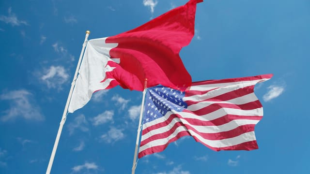 Flags of Bahrain and the United States waving against a bright blue sky, symbolizing international relations.