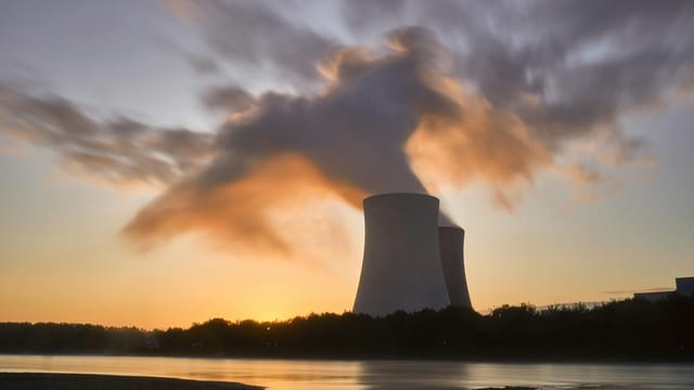 Dramatic image of a nuclear power plant at sunrise with steam rising into a colorful sky.