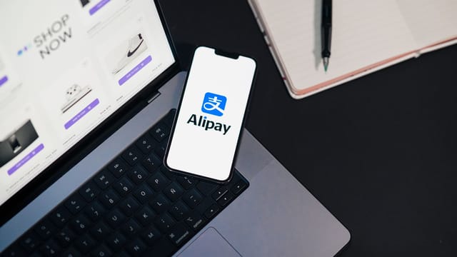 Smartphone displaying Alipay app on open laptop with online shopping site.