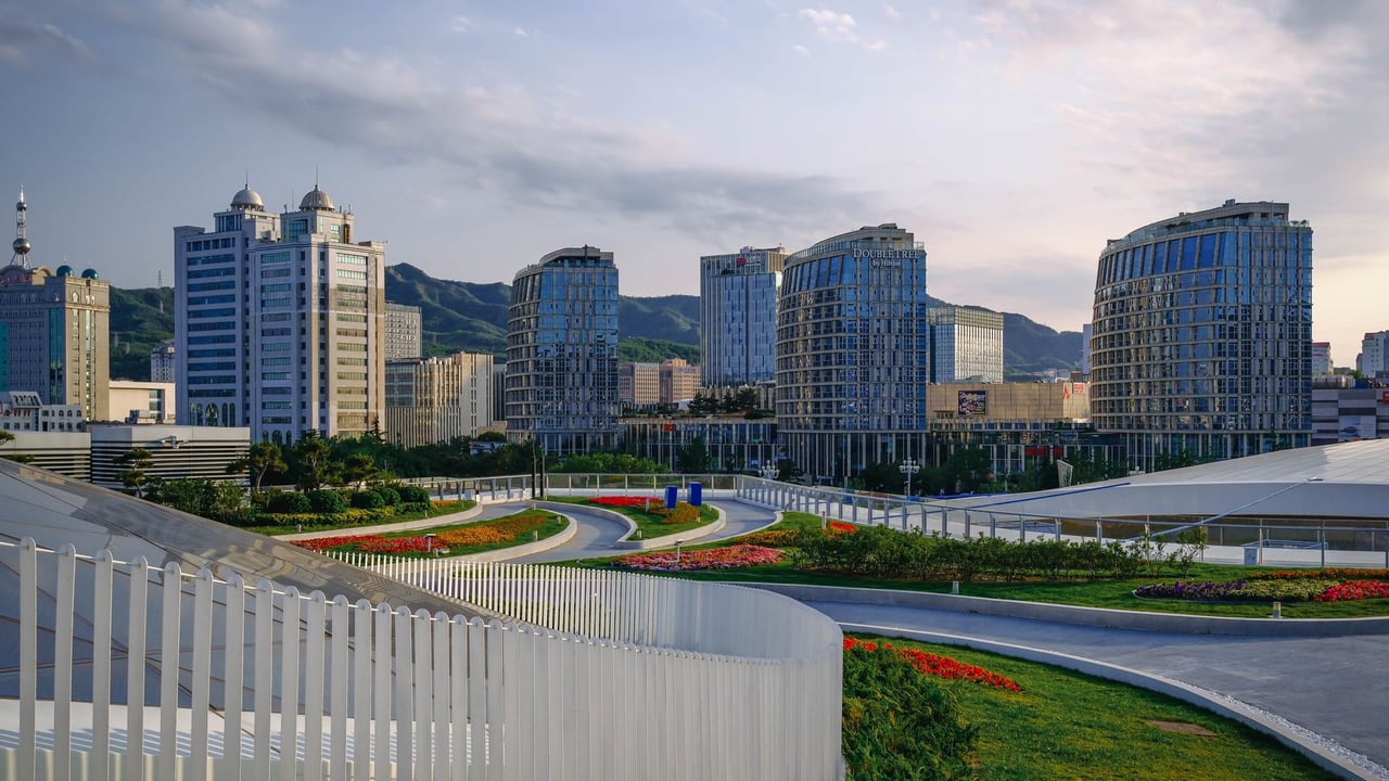 A scenic view of modern architecture buildings surrounded by greenery and vibrant flower beds under a cloudy sky.