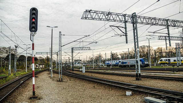 A modern train station with multiple tracks, trains, and a prominent signal under a cloudy sky.