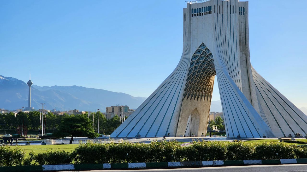 Capture of the iconic Azadi Tower in Tehran with a mountainous backdrop and clear sky.