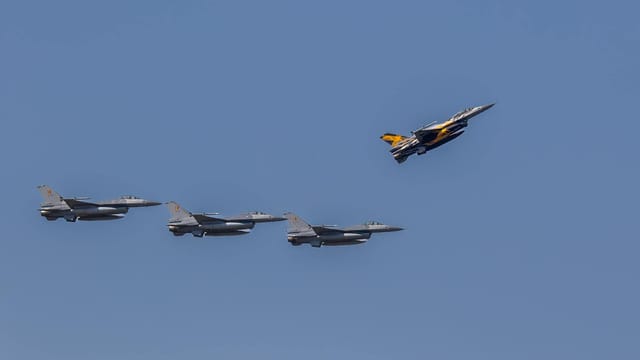Aerial view of F-16 fighter jets flying in formation against a clear blue sky.