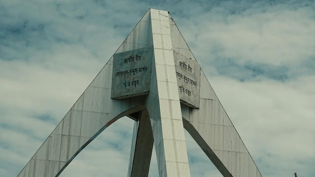A striking view of the Shaheed Minar monument in Sylhet against a cloudy blue sky.