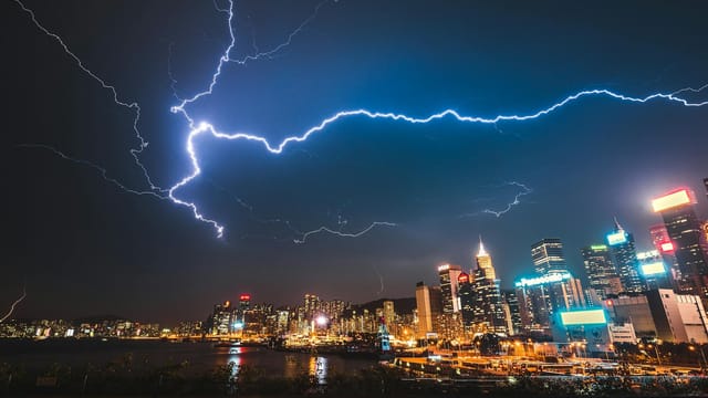 A striking image of a city skyline illuminated by a powerful lightning storm at night.