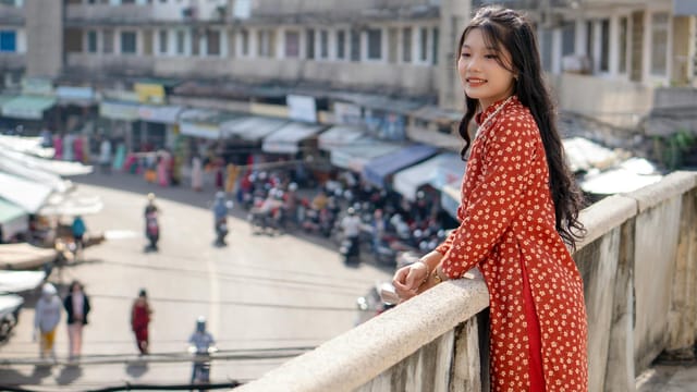 Woman in red floral dress standing on city bridge, smiling and posing.