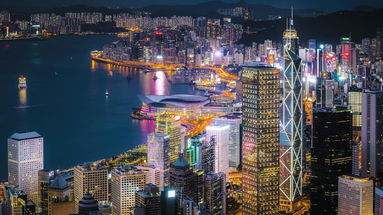 A stunning view of Hong Kong's illuminated skyline at night, showcasing iconic skyscrapers and a bustling harbor.