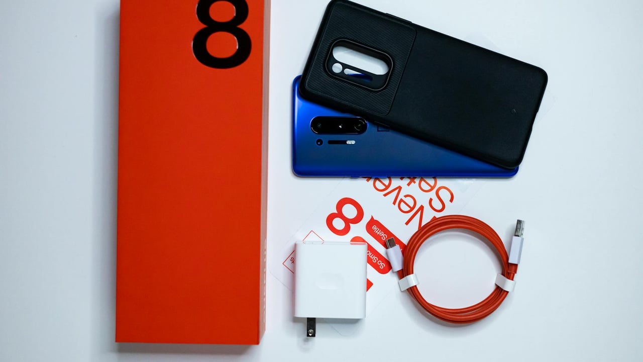 Flatlay of OnePlus 8 Pro with accessories on white background, showcasing packaging and contents.