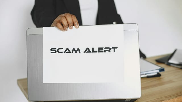 Business person holding a scam alert sign over a laptop, warning against online fraud.
