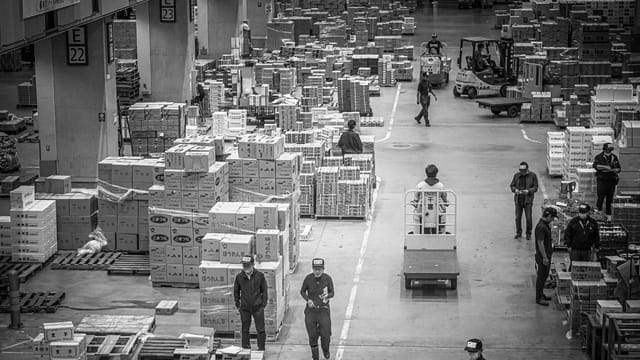 Black and white photograph of a bustling warehouse in Japan, featuring workers organizing and moving packages.