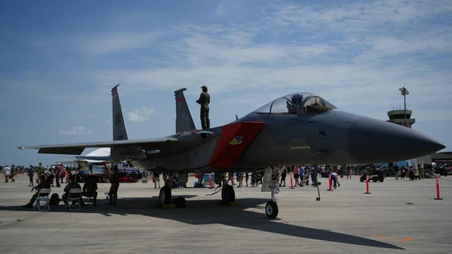 An F-15 fighter jet showcased at a Virginia air force base with a vibrant crowd and clear sky.