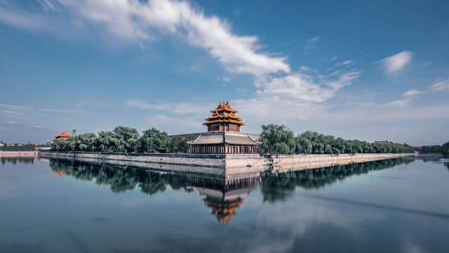 A stunning aerial view of the Forbidden City in Beijing with clear skies and calm waters reflecting the ancient architecture.
