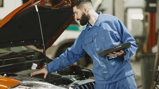 Professional mechanic examining a car engine under an open hood in a garage setting.