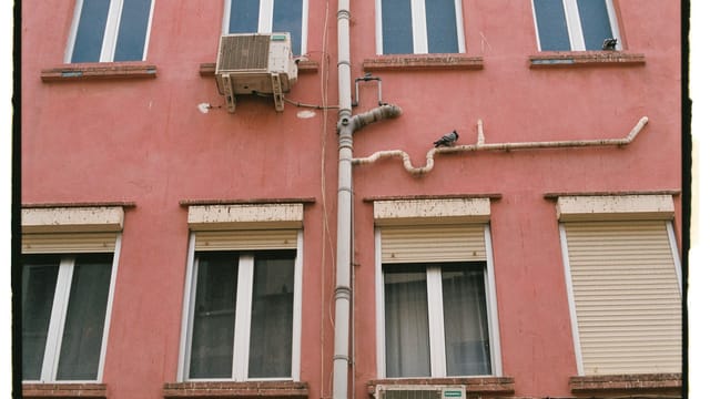 Close-up of a red residential building facade featuring windows and exposed pipes in Gibraltar.