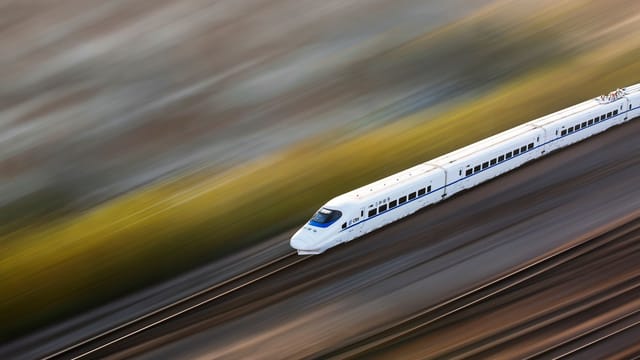 A sleek white high-speed train traveling at top speed, captured with a motion blur effect.