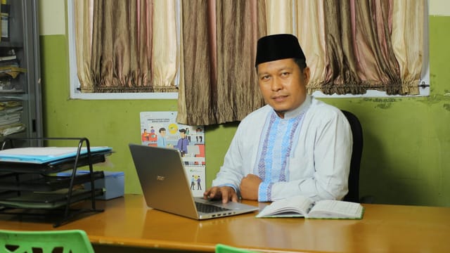 Successful Indonesian teacher working at a desk in a traditional outfit.