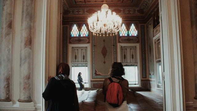 Visitors explore an ornate art museum hall with a stunning chandelier and detailed parquet flooring.