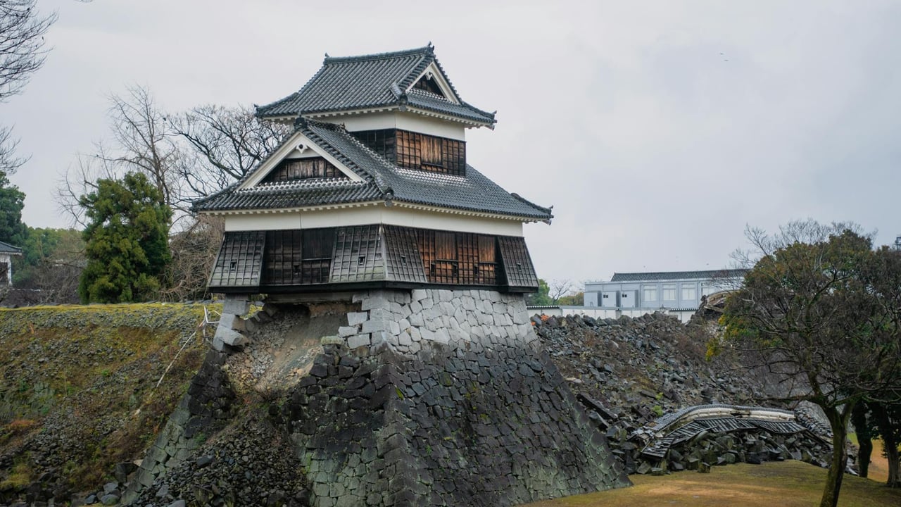 A damaged battlement of Kumamoto Castle amid a landscape of rubble and greenery.