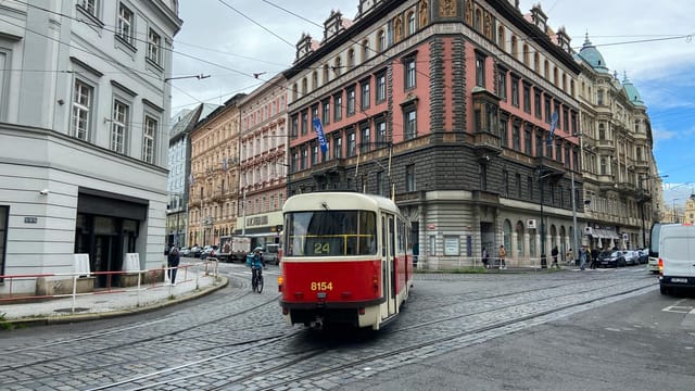 Iconic red tram navigates the charming streets of Prague, capturing urban life.