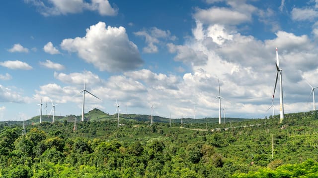 Scenic view of wind turbines on lush green hills, symbolizing renewable energy under a partly cloudy blue sky.