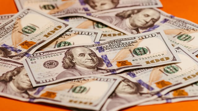 Scattered US $100 bills on a vibrant orange surface symbolizing wealth and finance.