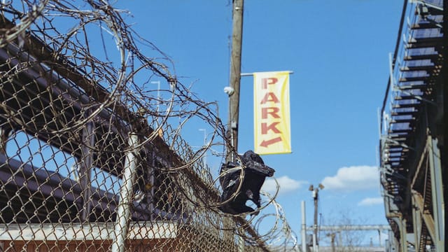 Chain-link fence with barbed wire under clear blue sky in NYC.