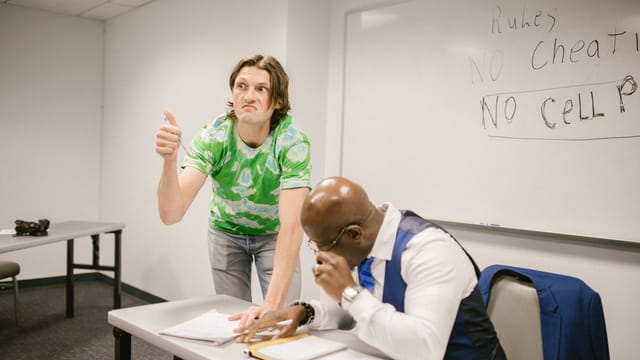 A teacher catches a student attempting to cheat with a hand signal during a classroom exam.