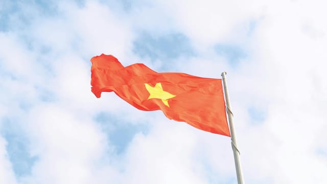 The vibrant red flag of Vietnam with a yellow star waves under a clear blue sky.