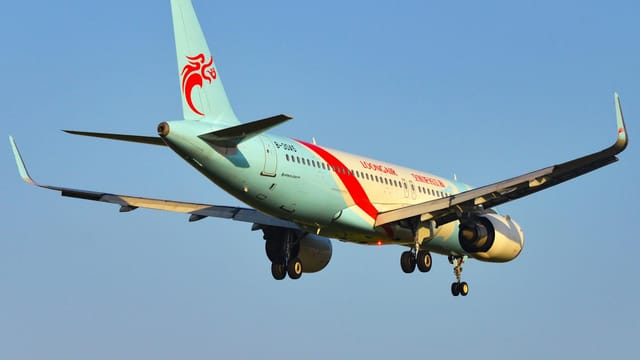 A commercial airplane descending for landing under a clear blue sky in Ningbo, China.