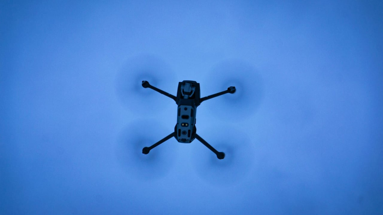 A drone seen flying in a clear blue sky, captured from below with motion blur on the rotors.
