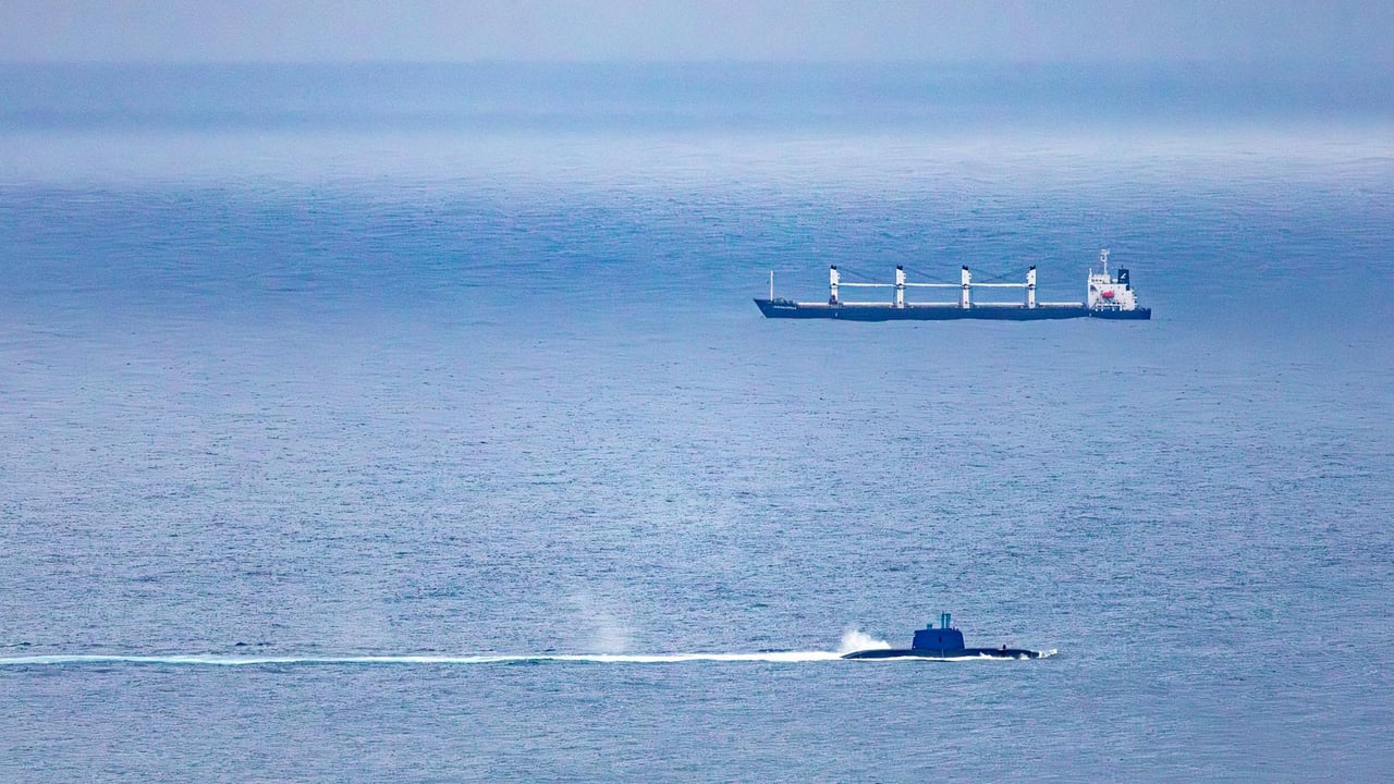 A cargo ship and submarine navigate the vast, open ocean under a clear sky.