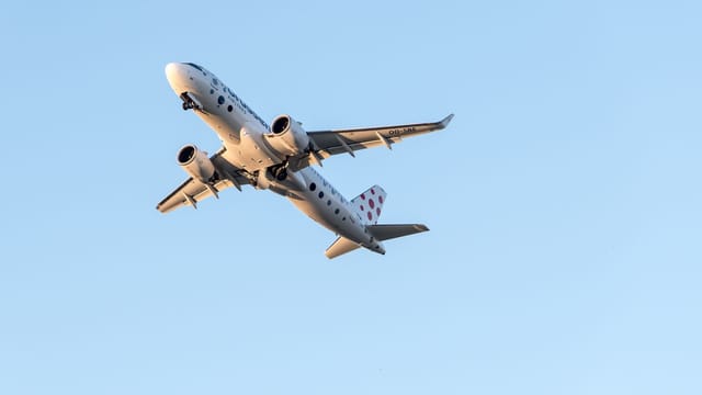 A commercial jet airplane flying high above Prague on a clear day, showcasing aviation travel.