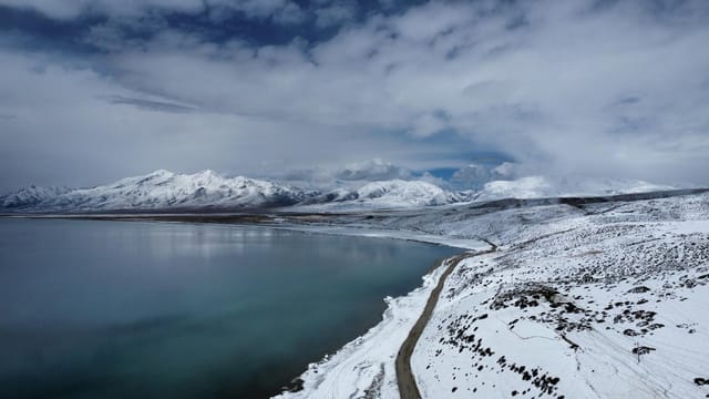 A serene winter scene in the Ngari Prefecture, Tibet, showcasing snow-covered mountains and a tranquil lake.