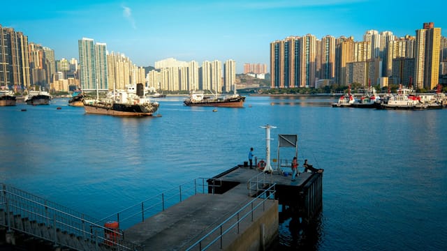Scenic view of Hong Kong's bustling harbor with skyscrapers and boats under a clear sky.