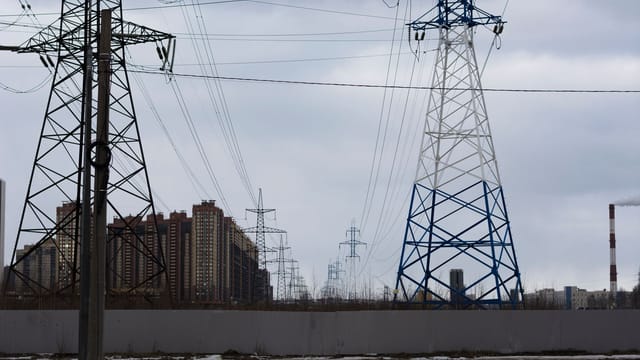 Cityscape featuring electricity pylons against a cloudy sky.